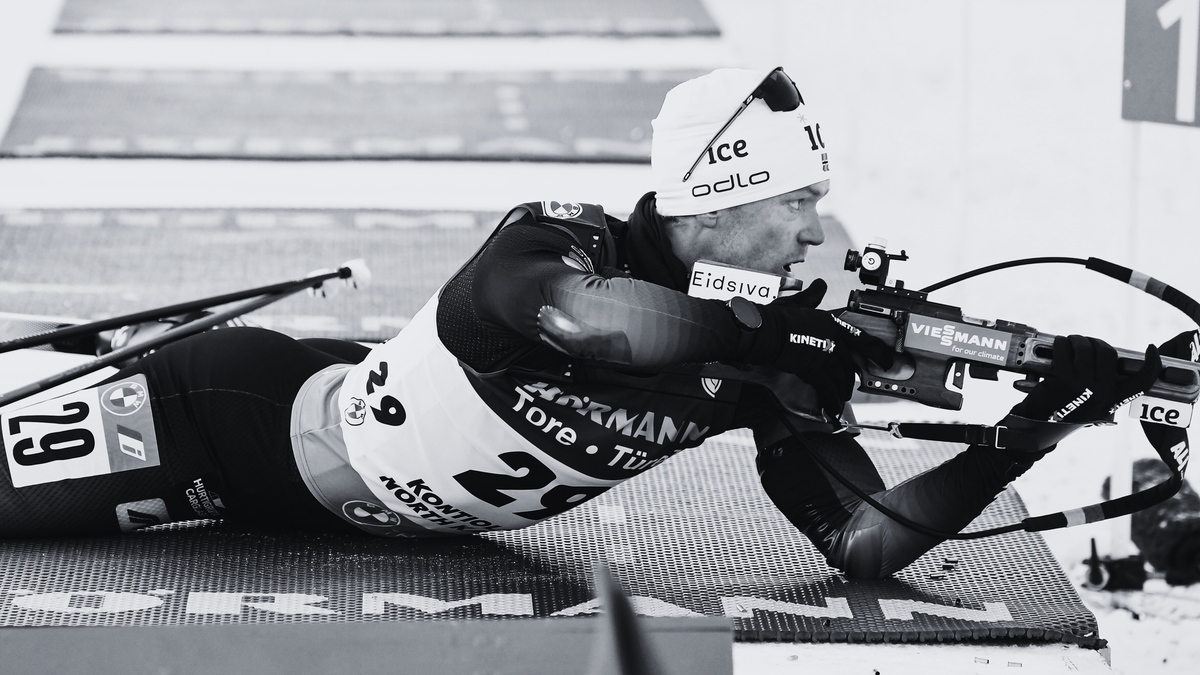 Biathlonista w pozycji leżącej celuje z karabinu na strzelnicy.