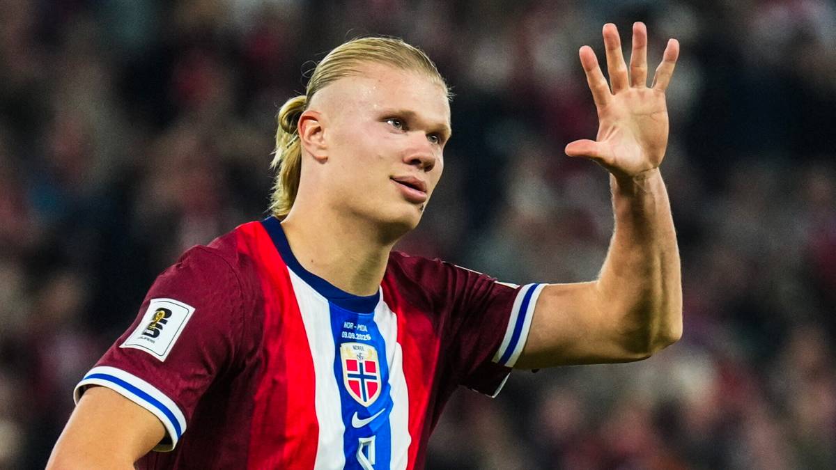 Piłkarz Erling Haaland w koszulce reprezentacji Norwegii unosi dłoń z wyciągniętymi pięcioma palcami.