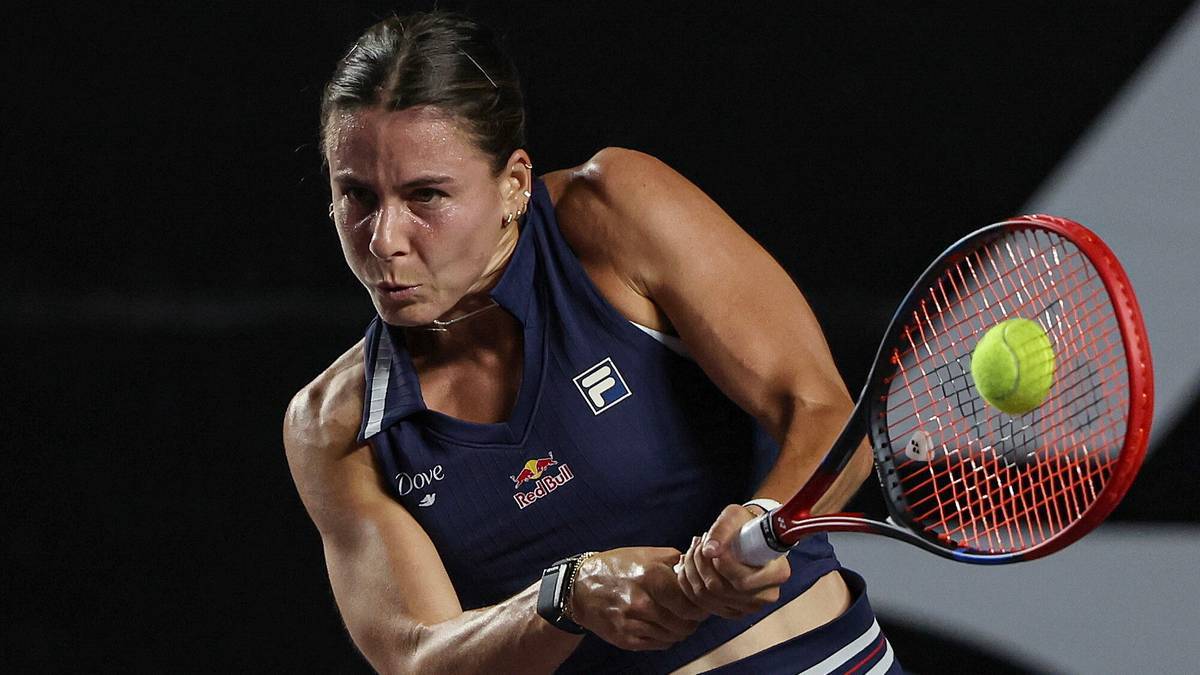 Tenisistka w ciemnoniebieskiej koszulce z logo Red Bull, w akcji, uderza piłkę rakietą.