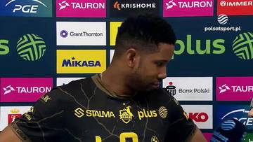 Wilfredo Leon, siatkarz, w czarnej koszulce z ż&oacute;łtymi zdobieniami, na tle baner&oacute;w sponsorskich.