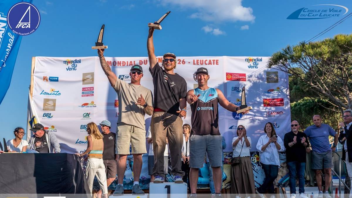 Trzech mężczyzn w strojach sportowych stoi na podium. Pierwszy z lewej, Maciek Rutkowski, trzyma puchar w uniesionej prawej ręce i wzbudza entuzjazm w tłumie. Na jego twarzy maluje się radość. Obok niego stoi Amado Vrieswijk, a trzeci zawodnik to Jordy Vonk. Wszyscy otrzymują gratulacje od zgromadzonych.