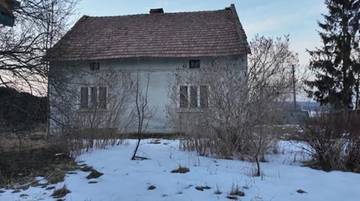 Zaniedbany dom jednorodzinny na tle zimowego krajobrazu.