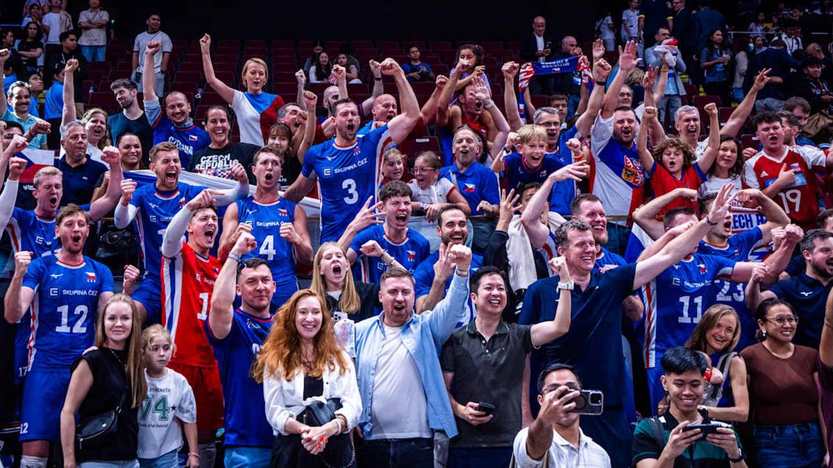 Grupa szczęśliwych siatkarzy w niebieskich strojach świętuje zwycięstwo, otoczona przez kibiców na trybunach.