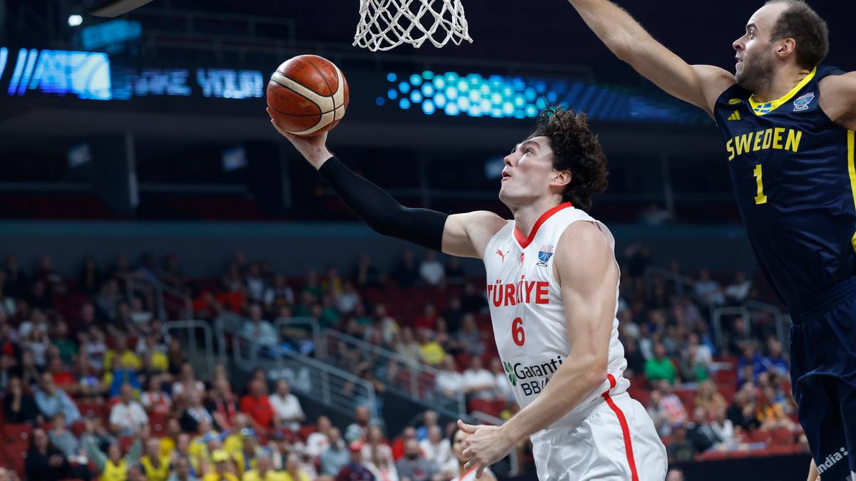 Koszykarz w białej koszulce z numerem 6 i napisem "TÜRKIYE" rzuca piłkę do kosza, podczas gdy drugi zawodnik w żółto-niebieskiej koszulce próbuje go zablokować.