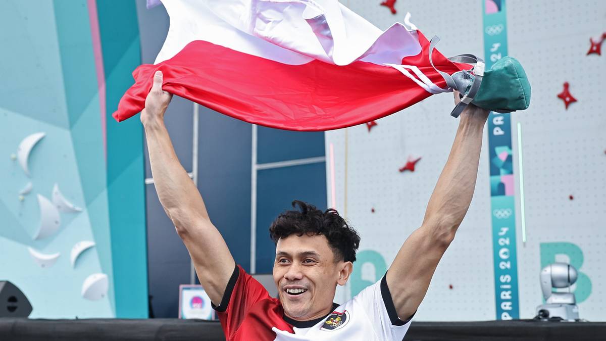 Mężczyzna trzyma w g&oacute;rze biało-czerwoną flagę Polski, świętując medal.