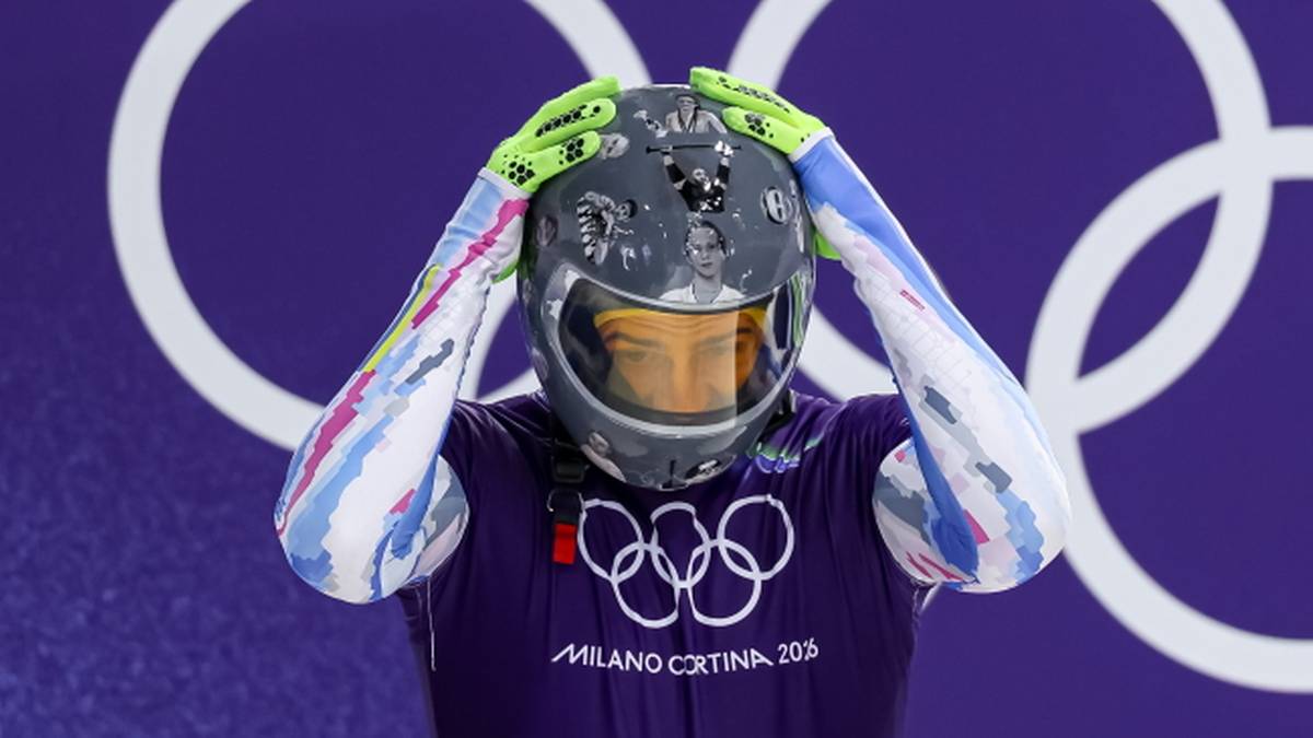 Skeletonista Vladyslav Heraskewycz w kasku przed pierścieniami olimpijskimi.