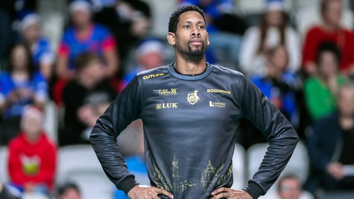 Mężczyzna w koszulce z logotypami klubowymi, z dłońmi na biodrach.