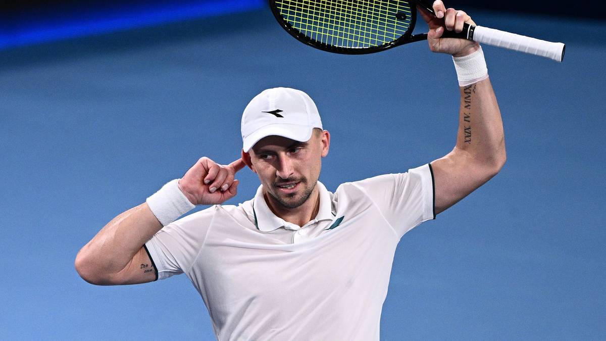 Tenisista Jan Zieliński w białej koszulce i czapce z daszkiem z białym daszkiem, podnoszący rakietę tenisową nad głową.