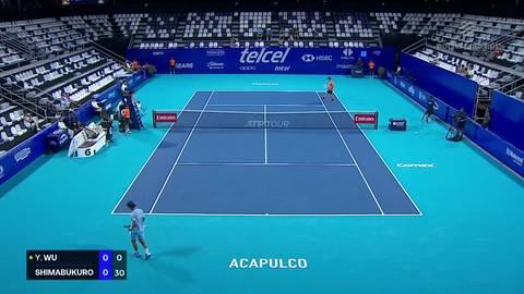 Kort tenisowy podczas meczu z widocznymi graczami, trybunami i tablicą wynik&oacute;w.