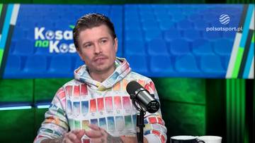 Mężczyzna w bluzie z kapturem z kolorowym wzorem siedzi przed mikrofonem.