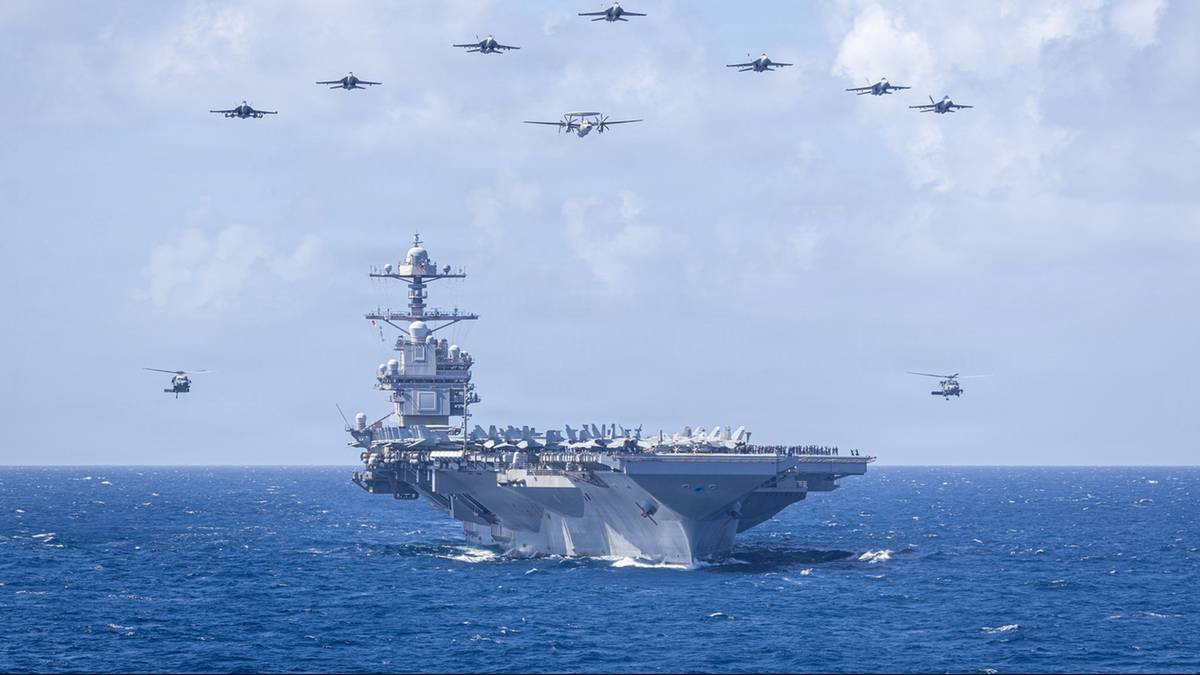 Lotniskowiec z samolotami formującymi się nad nim na niebie.