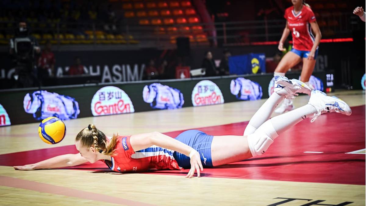 Zawodniczka siatkówki w kolorowym stroju sportowym w poślizgu na boisku zbliża się do piłki.