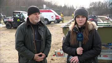 Mężczyzna i kobieta stoją na zewnątrz, w tle widać pojazdy ratownicze i sprzęt. Kobieta trzyma mikrofon z logo "EuroPAPATV".