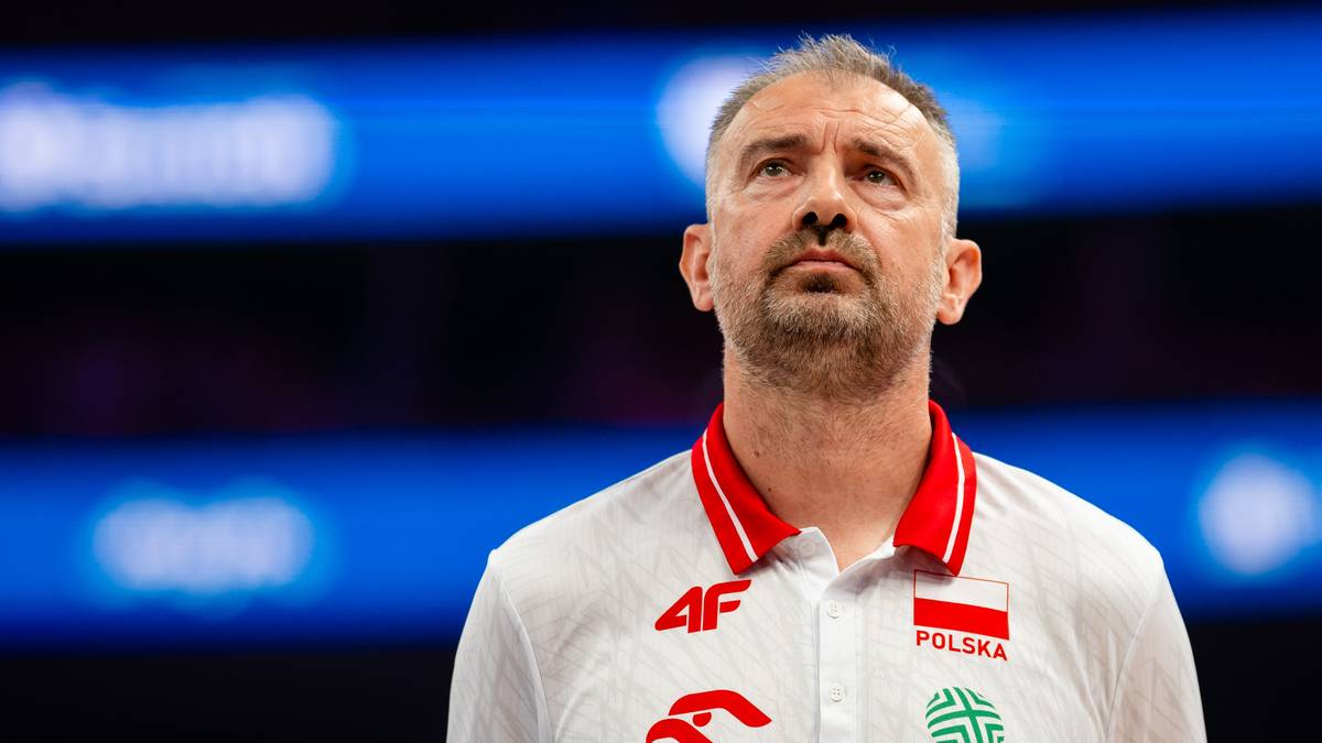 Portret mężczyzny o krótkich włosach i kilkudniowym zaroście, ubranego w białą koszulkę polo z czerwonymi elementami przy kołnierzu i rękawach. Na piersi widnieje logo "4F" oraz biało-czerwona flaga Polski z napisem "POLSKA". Tło jest niebieskie i rozmyte, sugerujące oświetlenie hali sportowej.