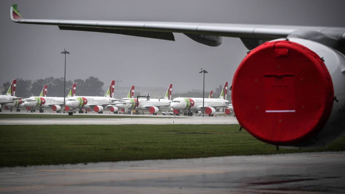 Fragment silnika samolotu z czerwonym elementem na pierwszym planie, w tle rząd zaparkowanych samolotów.