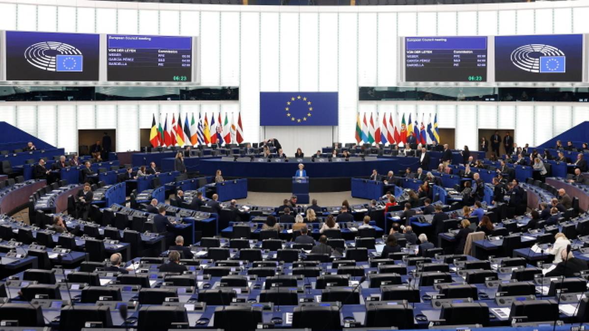 Sala plenarna Parlamentu Europejskiego z europosłami na miejscach i flagami państw członkowskich UE.