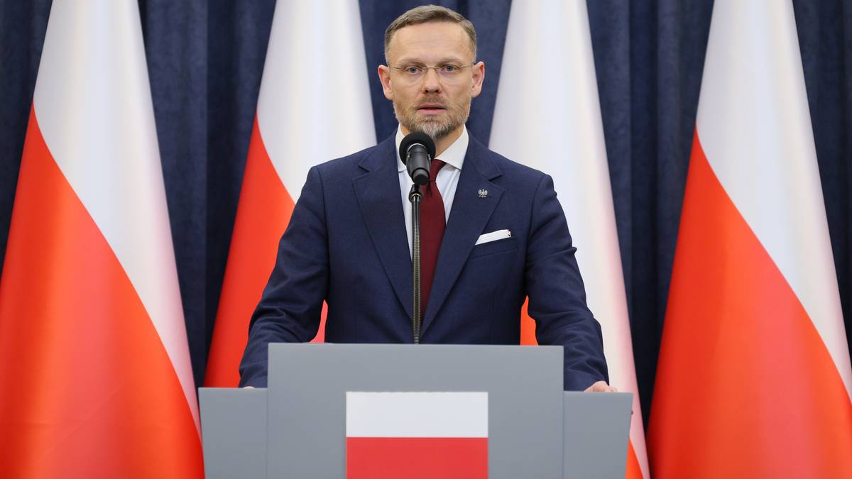 Zbigniew Bogucki przemawia za mównicą przed flagami Polski.