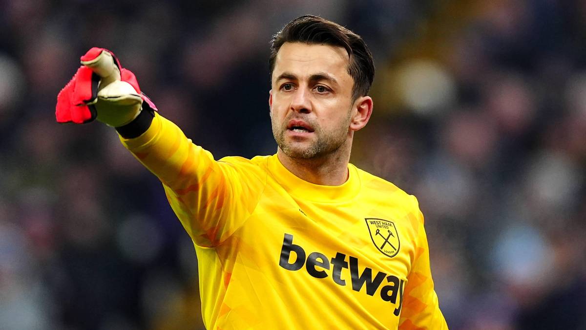 Piłkarz w żółtej koszulce bramkarskiej z logo "betway" i herbem klubu, patrzący w bok z uniesioną rękawicą.