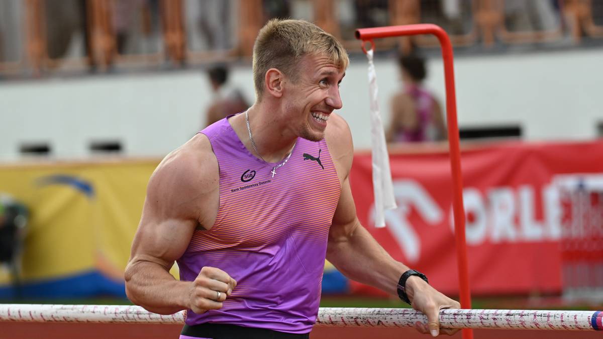 Uśmiechnięty tyczkarz Piotr Lisek w koszulce z numerem startowym podczas zawodów lekkoatletycznych.