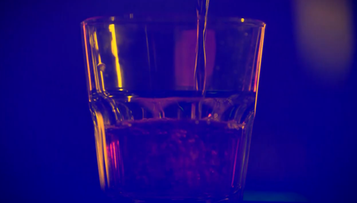 Szklanka z ciemnym płynem, do kt&oacute;rej nalewany jest kolejny płyn.