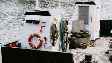 Widok zbliżenia na fragmenty dw&oacute;ch białych łodzi z linami i kołem ratunkowym, zacumowanych przy drewnianym pomoście.