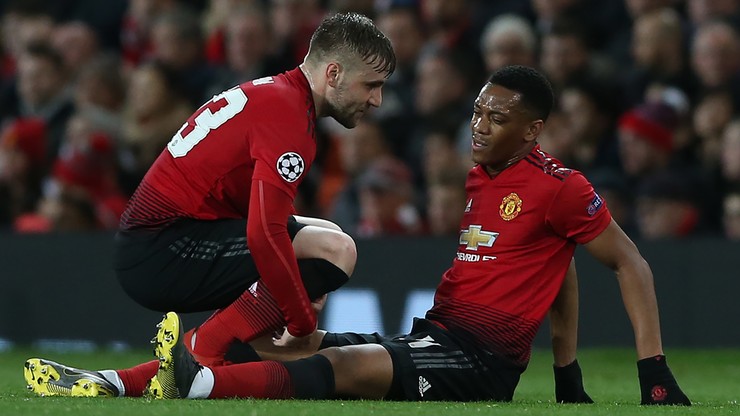 Dwóch piłkarzy Manchesteru United w czerwonych koszulkach. Jeden podtrzymuje drugiego, który siedzi na trawie i trzyma się za nogę.