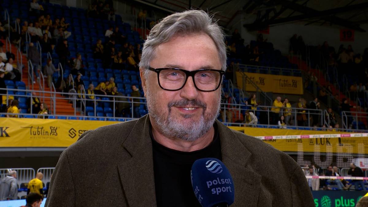 Mężczyzna w okularach i brązowej marynarce z mikrofonem Polsat Sport.