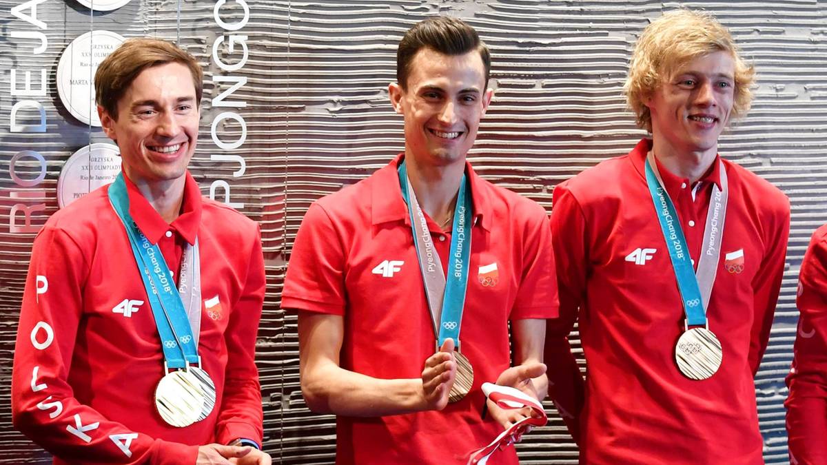 Prezydent Andrzej Duda stoi obok czterech polskich skoczków narciarskich w czerwonych strojach, prezentujących swoje medale.