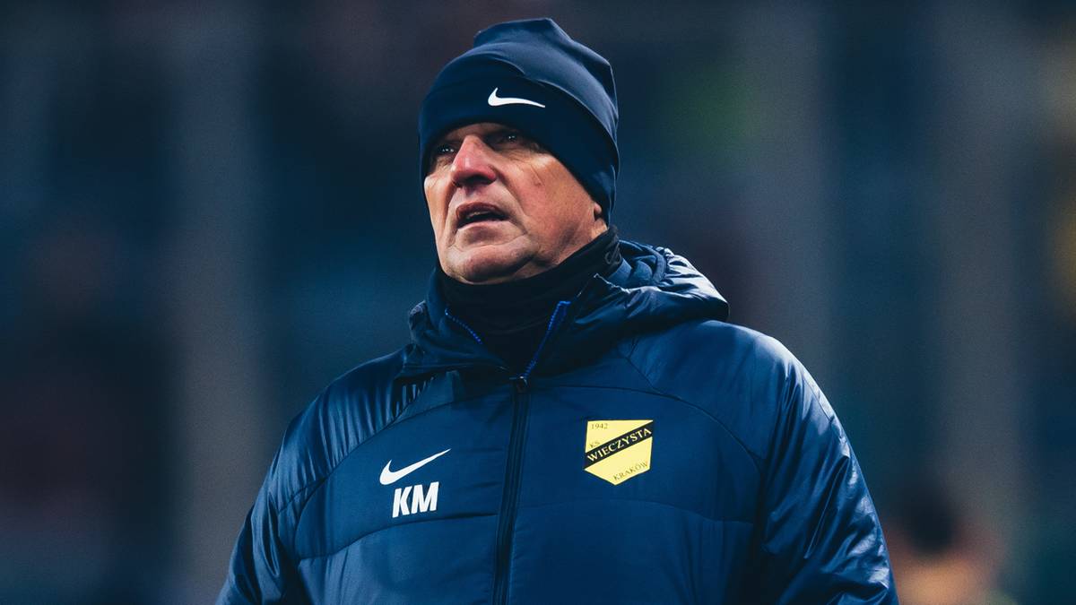 Mężczyzna w zimowej kurtce i czapce na tle stadionu.