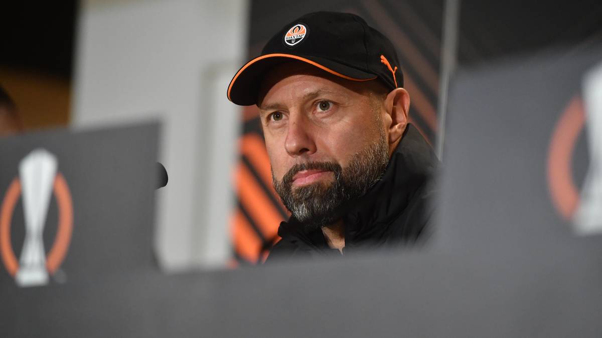 Portret mężczyzny w czapce z daszkiem z logo klubu piłkarskiego, z zarostem, podczas konferencji prasowej.