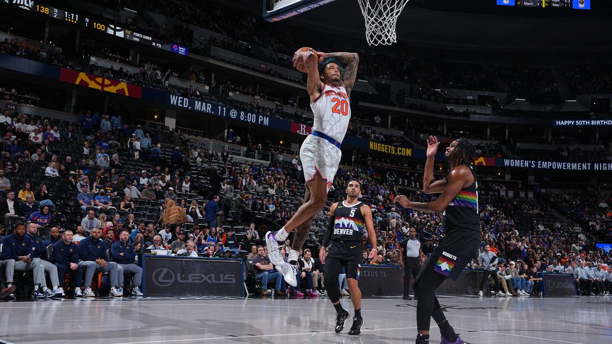 Gracz koszyk&oacute;wki w białej koszulce wykonuje wsad do kosza, w tle trybuny pełne widz&oacute;w.