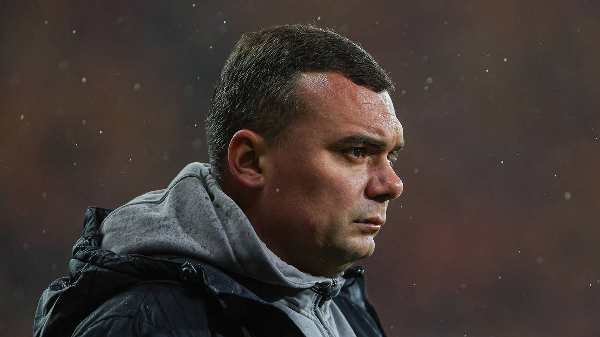 Portret Adriana Siemienieca, trenera piłkarskiego, z profilu, podczas meczu na stadionie. Ma krótkie włosy i poważny wyraz twarzy, ubrany jest w kurtkę i bluzę z kapturem.