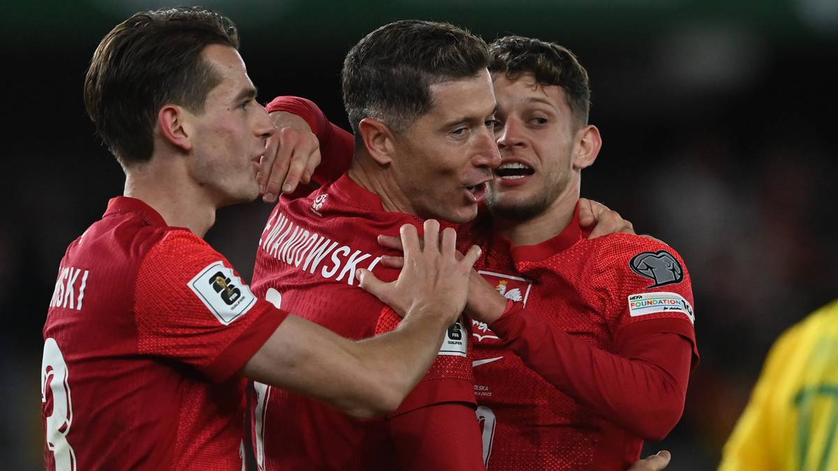 Trzech piłkarzy w czerwonych koszulkach reprezentacji Polski, dwóch obejmuje trzeciego, który jest w środku, prawdopodobnie po strzeleniu bramki.