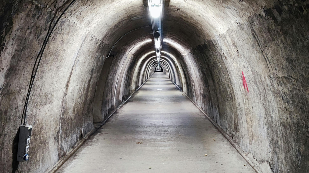 Długi, oświetlony tunel o łukowatym sklepieniu.
