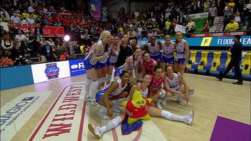 Siatkarki Imoco Volley Conegliano świętujące zwycięstwo, siedzące na parkiecie z pucharem.