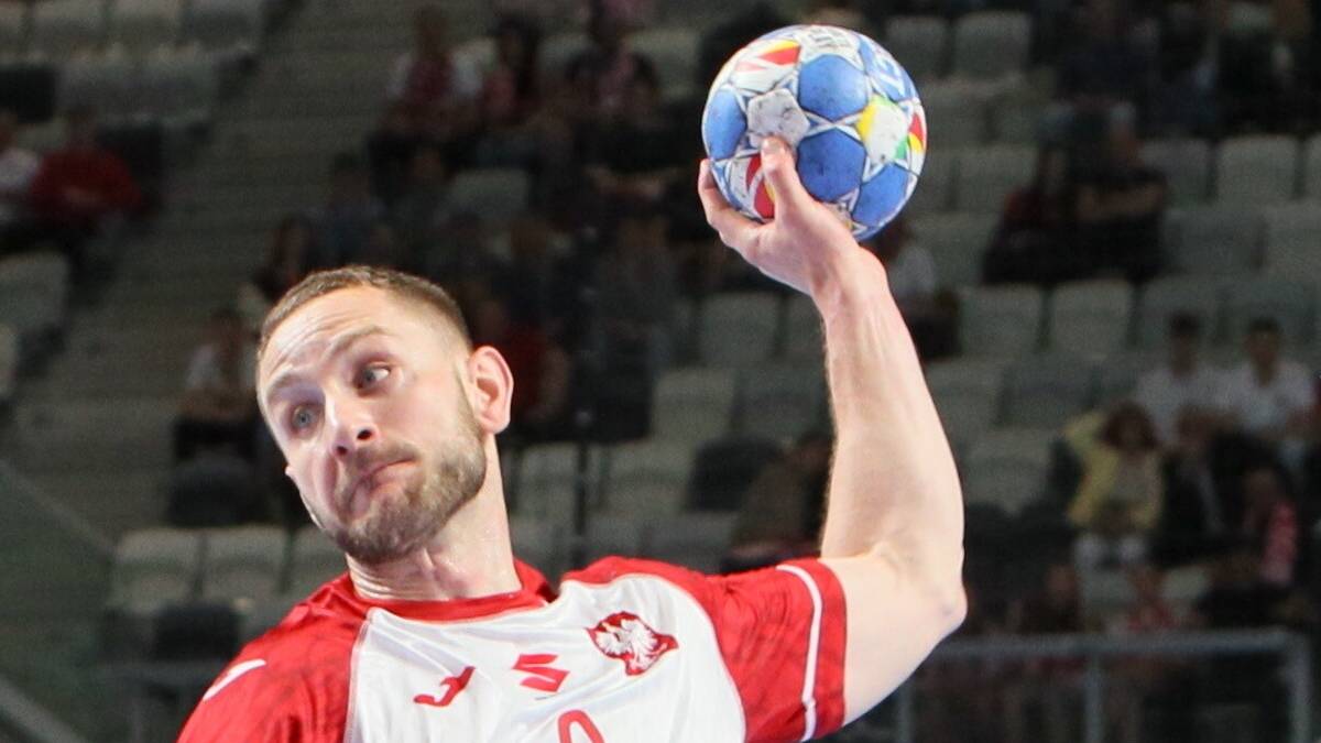 Piłkarz ręczny w białej koszulce z czerwonymi detalami i numerem 3 wykonuje rzut do bramki.