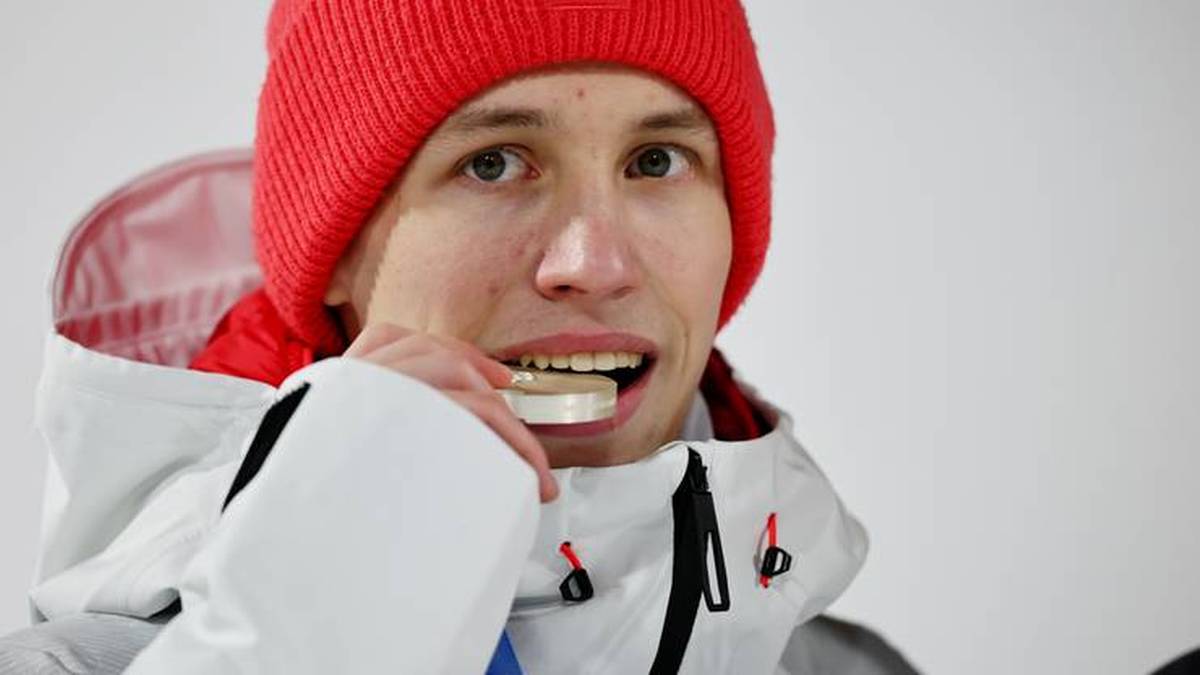 Młody mężczyzna w czerwonej czapce i sportowej kurtce trzyma w ustach biały przedmiot.