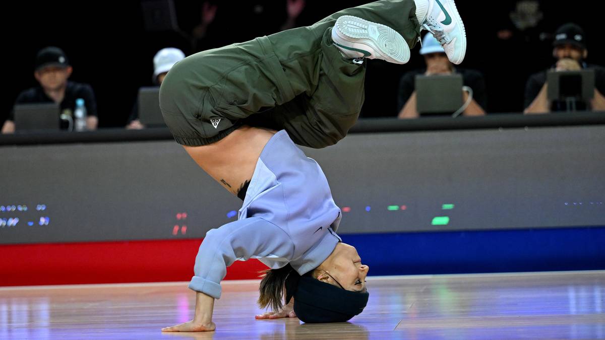 Tancerz wykonujący figurę breakdance'ową stojąc na rękach z nogami zgiętymi w kolanach.