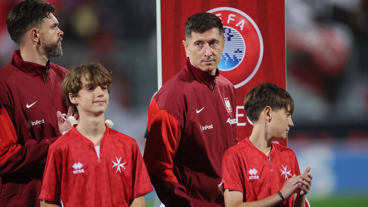 Trener i młodzi zawodnicy w strojach reprezentacji Malty z logo UEFA w tle.