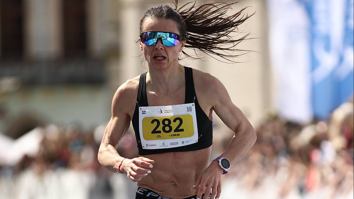 Biegaczka w ciemnej koszulce sportowej i spodenkach, z numerem startowym 282, biegnie na zawodach na zewnątrz, z włosami rozwianymi na wietrze.