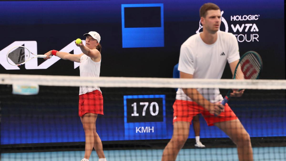 Tenisistka Iga Świątek serwuje, obok niej stoi tenisista, na ekranie w tle widnieje wynik.