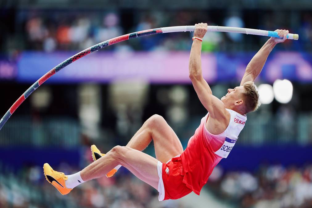 Dłonie sportowca trzymające tyczkę nad głową.