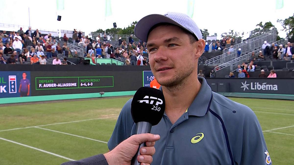 Kamil Majchrzak udziela wywiadu na korcie tenisowym, trzymając mikrofon ATP.