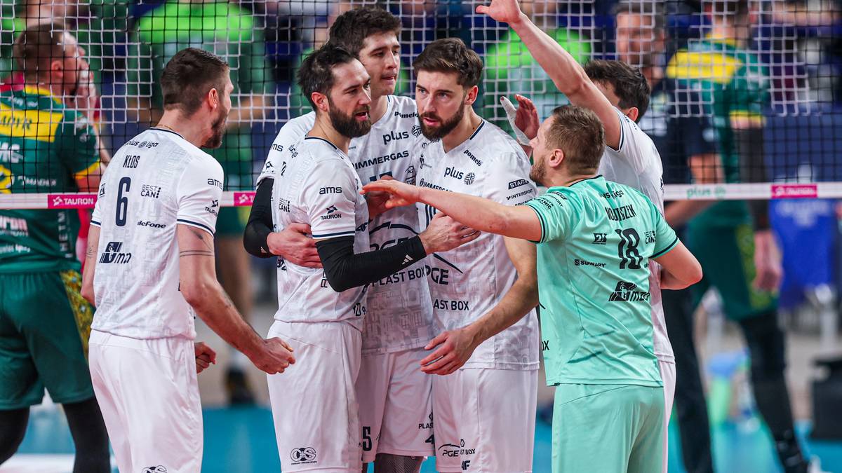 Grupa siatkarzy w białych strojach cieszy się wsp&oacute;lnie na boisku, z innymi zawodnikami w zielonych koszulkach w tle.