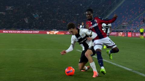 Dwóch piłkarzy walczy o piłkę na boisku, jeden w białej koszulce, drugi w czerwonej. Piłka znajduje się przed nimi.