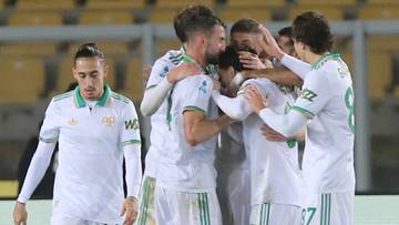 Piłkarze w białych strojach świętują razem na boisku piłkarskim.