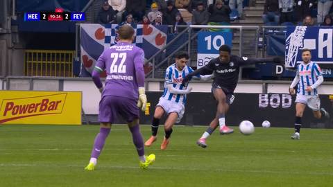 Fragment meczu piłki nożnej. Zawodnik w czarnym stroju prowadzi piłkę, atakowany przez dw&oacute;ch graczy w białych pasiasych koszulkach. Bramkarz w fioletowym stroju jest gotowy do interwencji.