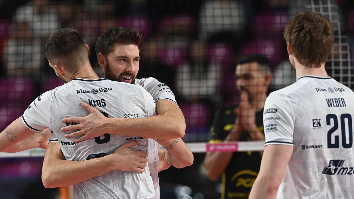 Siatkarze w białych koszulkach obejmują się na boisku, w tle widać inne osoby.