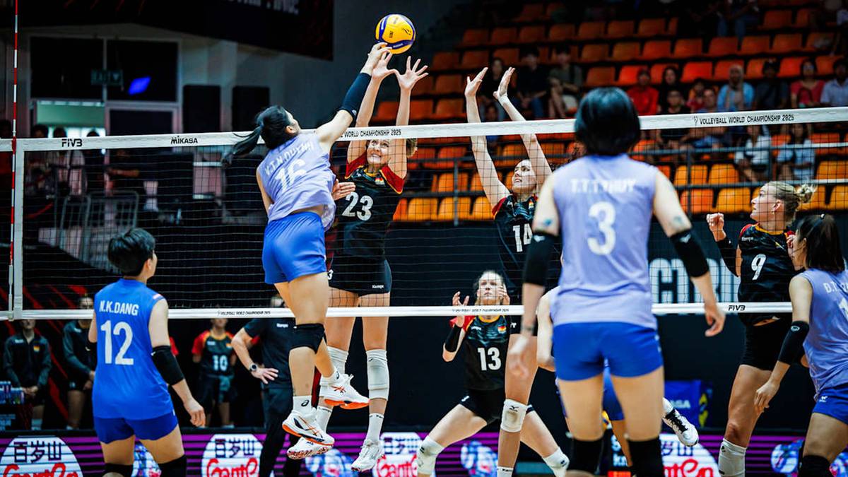 Siatkarka w niebieskim stroju odbija piłkę nad siatką, podczas gdy przeciwniczka w białym stroju próbuje ją zablokować.