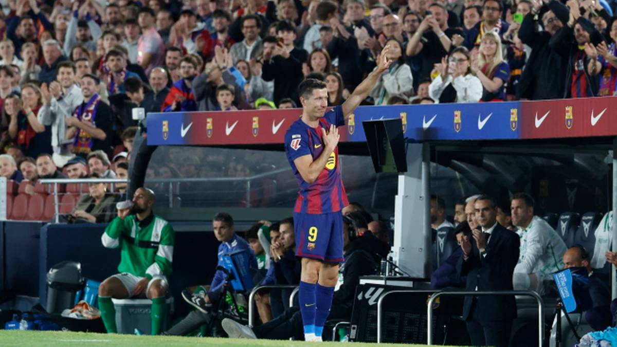 Piłkarz Robert Lewandowski w stroju FC Barcelony unosi rękę w geście triumfu, stojąc na murawie stadionu.